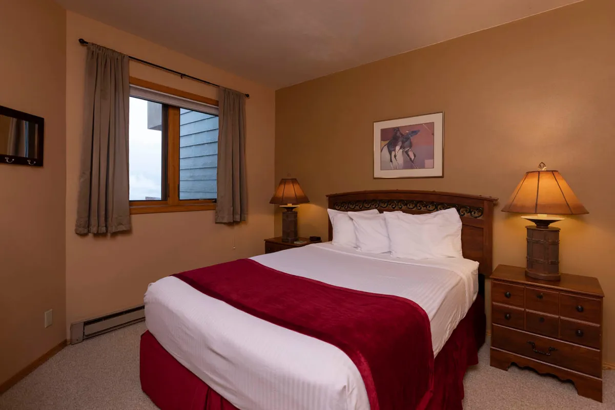 A welcoming bedroom scene with a neatly made bed, bedside lamps casting a gentle glow, a window letting in natural light, and tasteful wall art. The space feels private yet bright, perfect for reading or relaxing after a day outdoors.