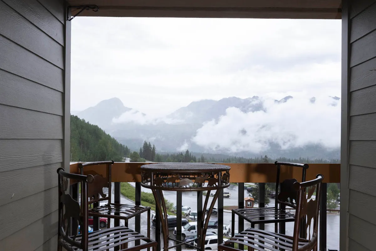 An inviting balcony with comfortable seating overlooks a sweeping view of mountains and drifting clouds. The tranquil outdoor setting evokes relaxation, perfect for unwinding after a day of adventure or sharing family moments while taking in the scenery.