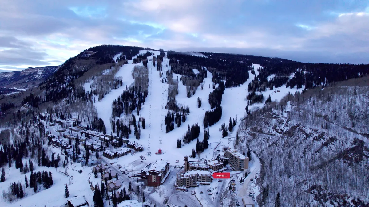 An inviting exterior scene of resort buildings framed by ski slopes and tall pine trees. The image evokes the excitement of outdoor activities with accessible trails and the welcoming atmosphere of the resort grounds.